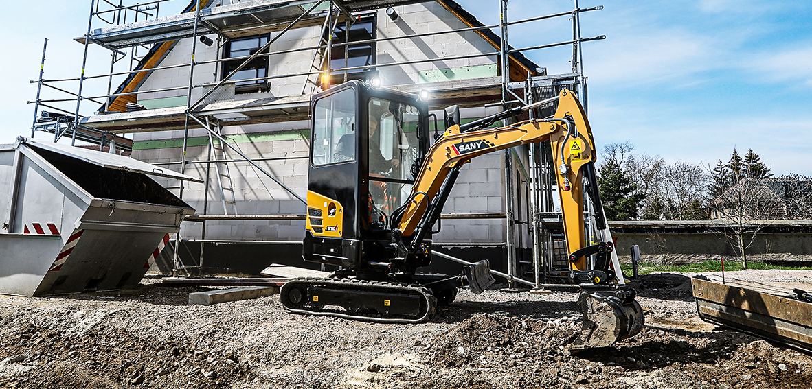 Gelber SANY SY18C Minibagger auf Raupen vor einem eingerüsteten Rohbau