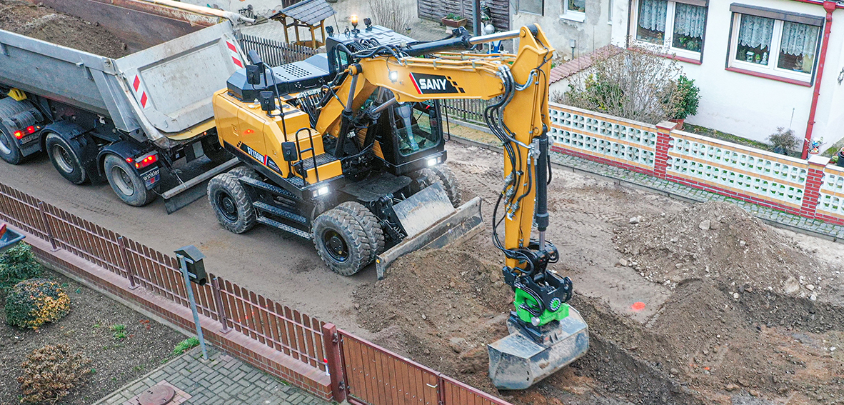 Gelber SANY SY155W Mobilbagger auf Rädern belädt einen Kipper auf einer Baustelle